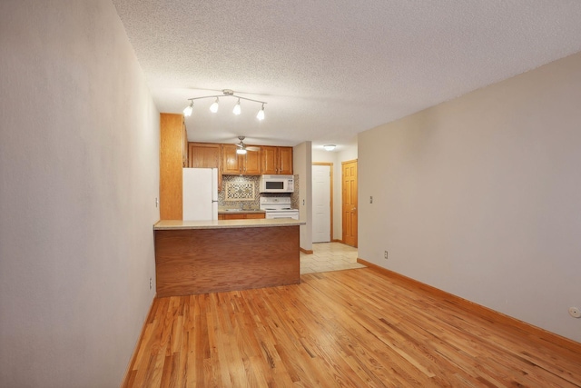 kitchen with light hardwood / wood-style flooring, a textured ceiling, kitchen peninsula, and white appliances