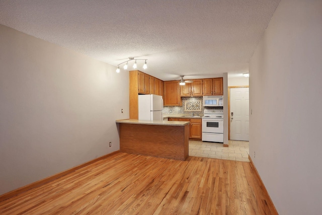 kitchen with kitchen peninsula, decorative backsplash, a textured ceiling, light wood-type flooring, and white appliances