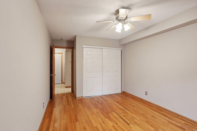 unfurnished bedroom featuring a closet, a textured ceiling, light wood-type flooring, and ceiling fan