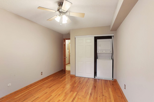 unfurnished bedroom featuring ceiling fan, a textured ceiling, light hardwood / wood-style flooring, stacked washer / drying machine, and a closet