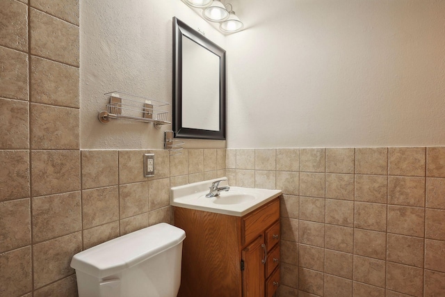 bathroom with toilet, vanity, and tile walls