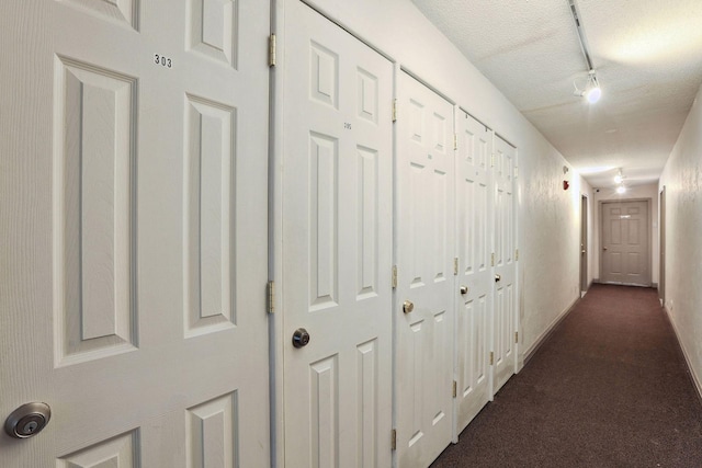 hallway featuring a textured ceiling and dark colored carpet