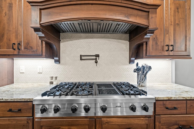 kitchen with custom range hood, backsplash, light stone counters, and stainless steel gas cooktop