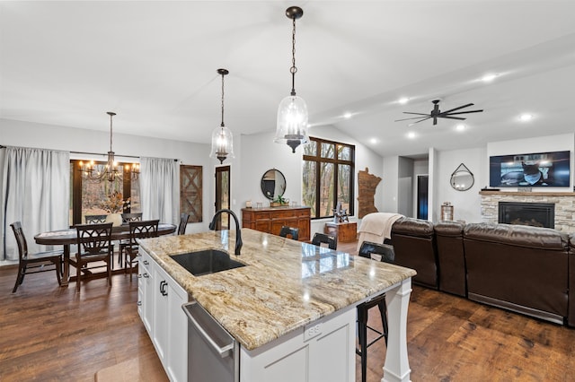 kitchen featuring a stone fireplace, white cabinetry, pendant lighting, and a kitchen island with sink