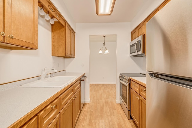 kitchen featuring light wood-type flooring, appliances with stainless steel finishes, a notable chandelier, hanging light fixtures, and sink