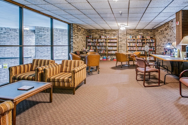 sitting room featuring expansive windows, a paneled ceiling, carpet flooring, and brick wall