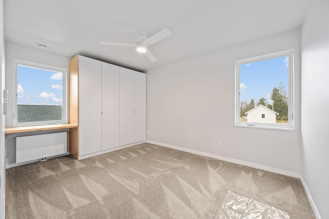 unfurnished bedroom featuring multiple windows, ceiling fan, radiator heating unit, and carpet floors