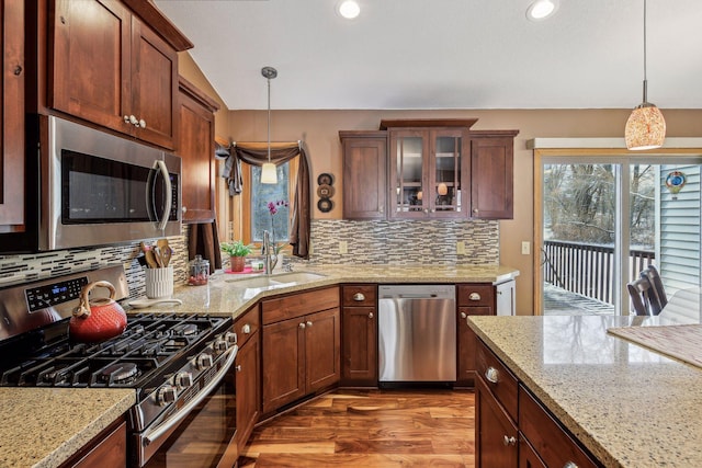 kitchen with dark wood-type flooring, pendant lighting, a sink, stainless steel appliances, and glass insert cabinets