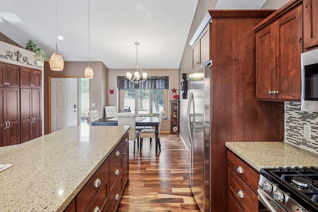 kitchen featuring wood finished floors, lofted ceiling, decorative backsplash, hanging light fixtures, and appliances with stainless steel finishes