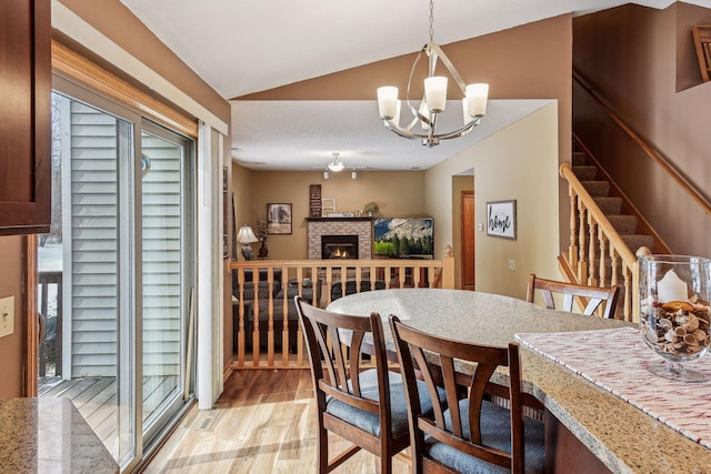 dining area with lofted ceiling, a fireplace, stairs, light wood-style floors, and a chandelier