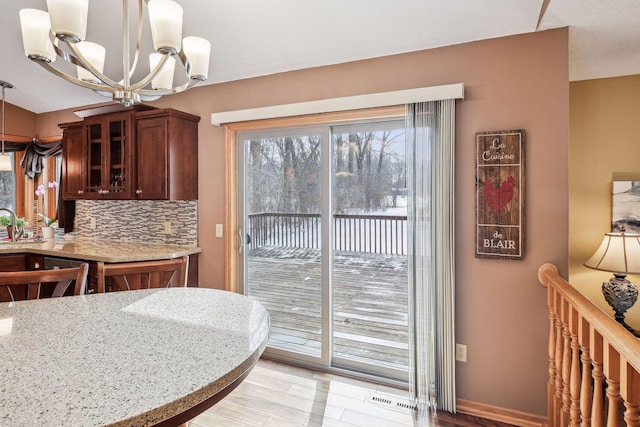 kitchen with light stone counters, visible vents, glass insert cabinets, pendant lighting, and backsplash