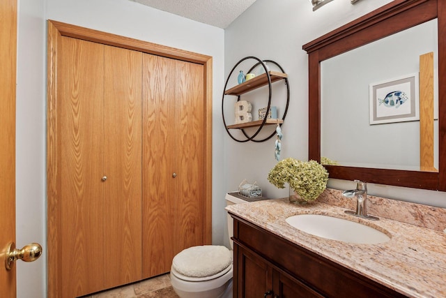 half bath featuring vanity, toilet, and a textured ceiling