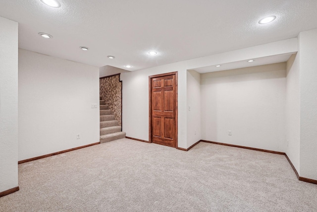 finished basement featuring stairway, baseboards, carpet floors, and a textured ceiling