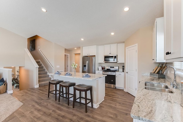 kitchen featuring a kitchen island, a breakfast bar area, wood finished floors, stainless steel appliances, and a sink