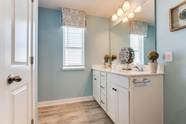 full bath featuring double vanity, a sink, baseboards, and wood finished floors