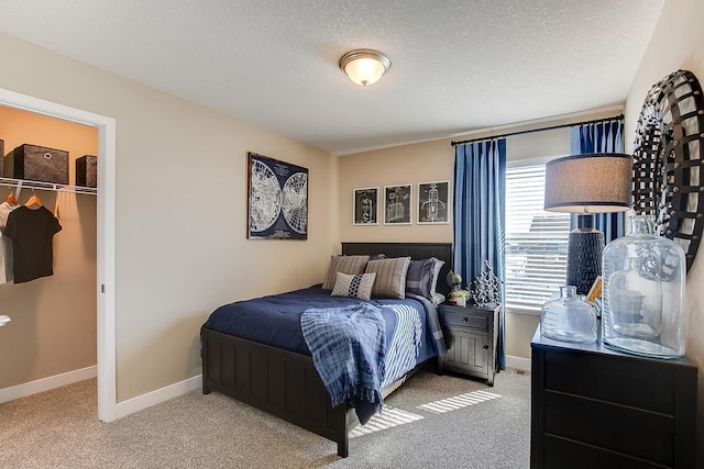 bedroom featuring a textured ceiling, a spacious closet, baseboards, and carpet flooring