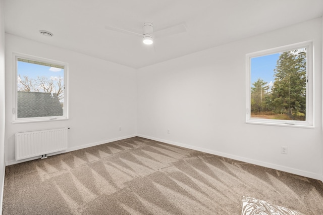 carpeted spare room with a wealth of natural light, ceiling fan, and radiator