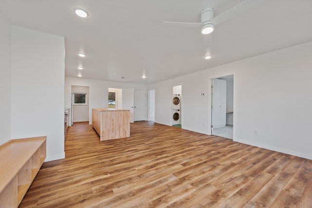 unfurnished living room with light hardwood / wood-style floors, ceiling fan, and stacked washer / drying machine