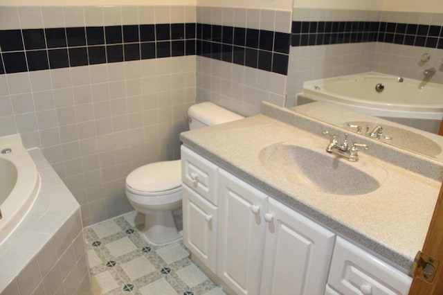 bathroom with vanity, tiled tub, tile walls, tile patterned flooring, and toilet