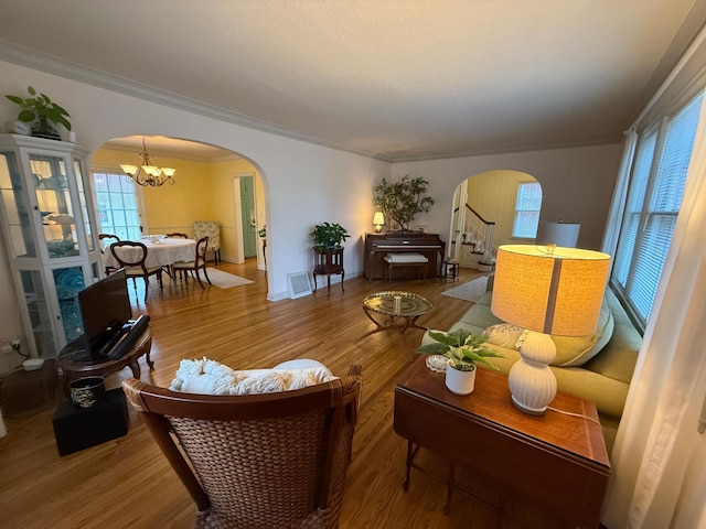 living room featuring wood-type flooring, ornamental molding, a wealth of natural light, and an inviting chandelier