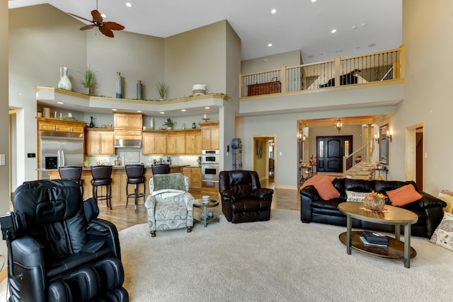 living room featuring a towering ceiling, ceiling fan, and light carpet