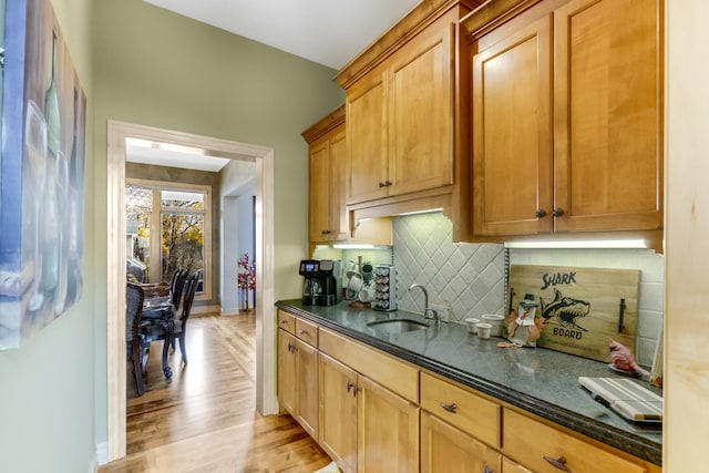 kitchen featuring dark stone countertops, sink, light wood-type flooring, and decorative backsplash