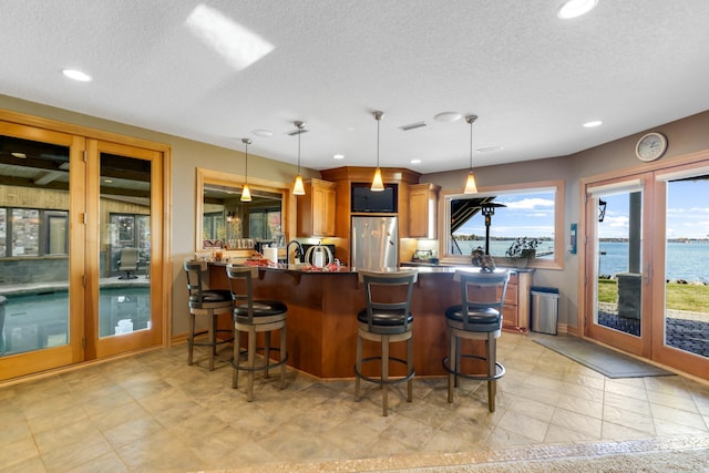 kitchen with kitchen peninsula, a water view, decorative light fixtures, and stainless steel fridge