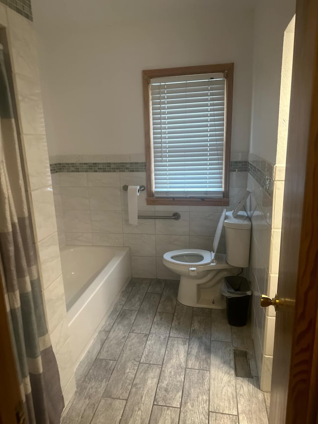 bathroom with a bathing tub, hardwood / wood-style floors, tile walls, and toilet