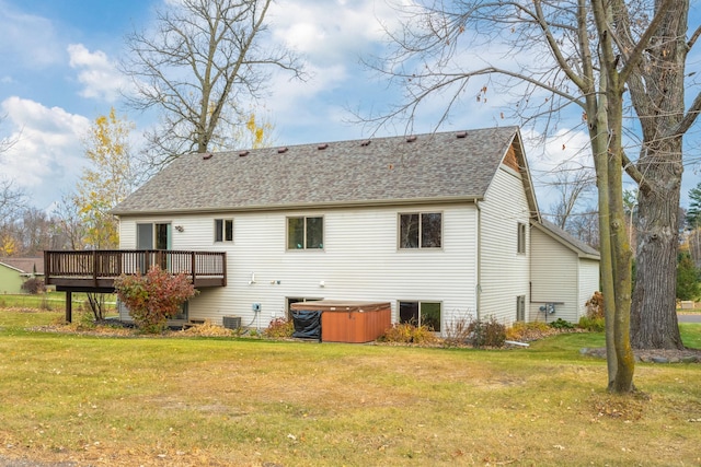 rear view of house featuring a hot tub, a wooden deck, and a lawn