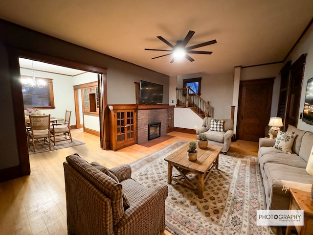 living room featuring ceiling fan with notable chandelier, light hardwood / wood-style floors, and a fireplace