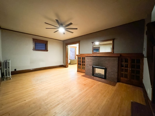 unfurnished living room with radiator, light wood-type flooring, ceiling fan, and a fireplace