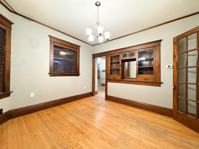 empty room featuring light hardwood / wood-style floors, a chandelier, and crown molding