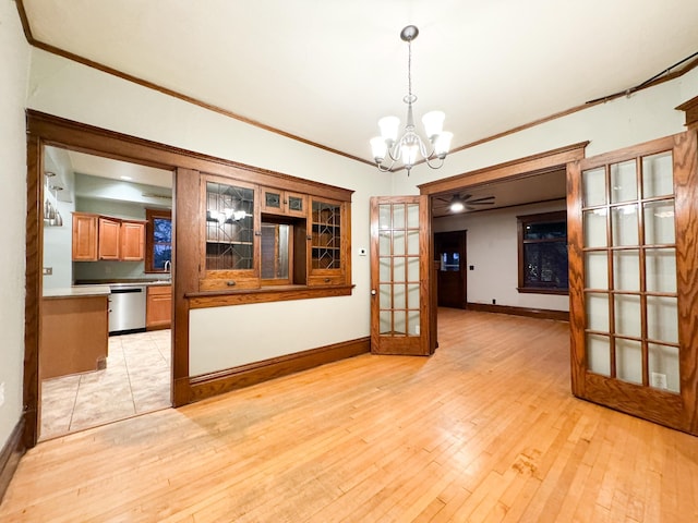 unfurnished dining area featuring french doors, crown molding, light wood-type flooring, sink, and ceiling fan with notable chandelier