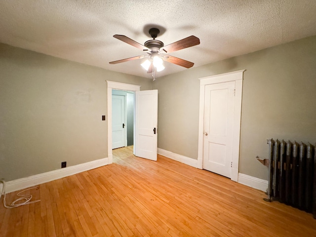 unfurnished bedroom featuring ceiling fan, a textured ceiling, radiator heating unit, and light wood-type flooring