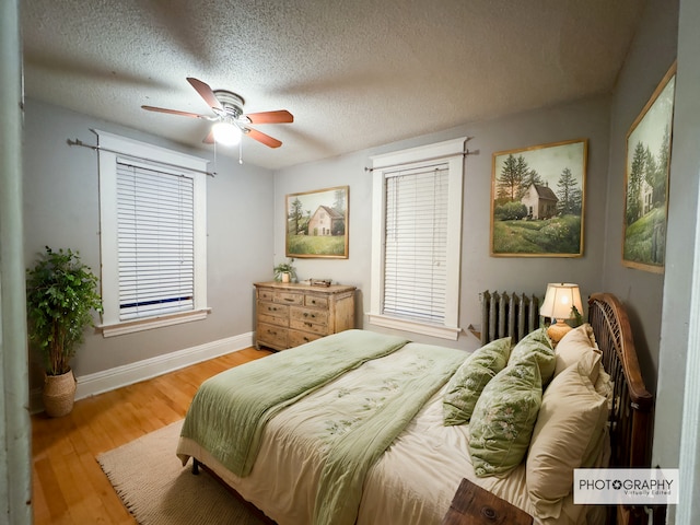 bedroom featuring radiator, ceiling fan, a textured ceiling, light hardwood / wood-style flooring, and multiple windows