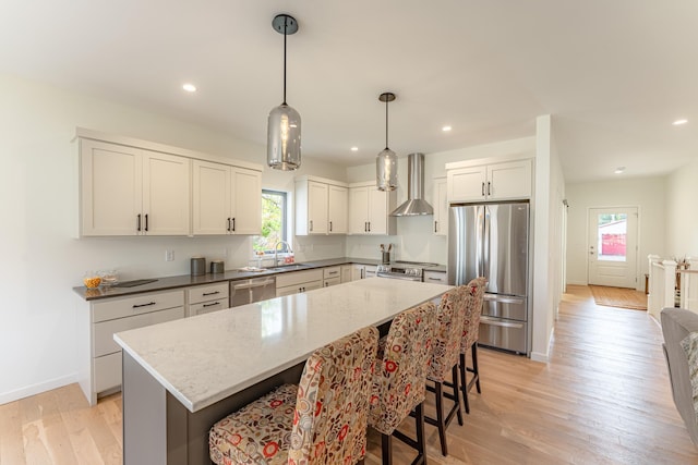 kitchen with white cabinets, wall chimney range hood, sink, a kitchen island, and stainless steel appliances