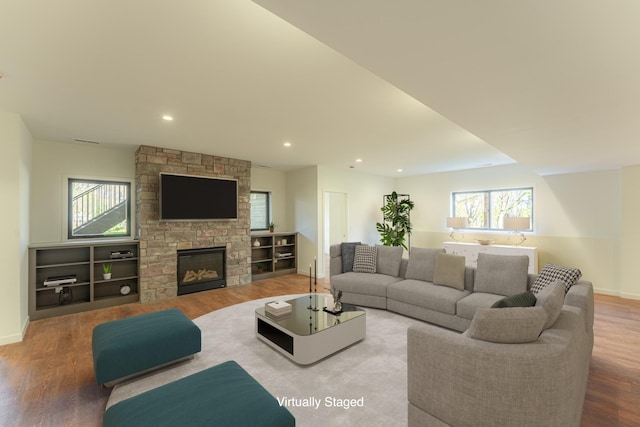 living room featuring a stone fireplace, plenty of natural light, and hardwood / wood-style flooring