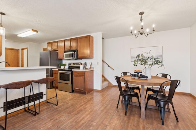 kitchen with decorative light fixtures, light hardwood / wood-style floors, a kitchen breakfast bar, and appliances with stainless steel finishes