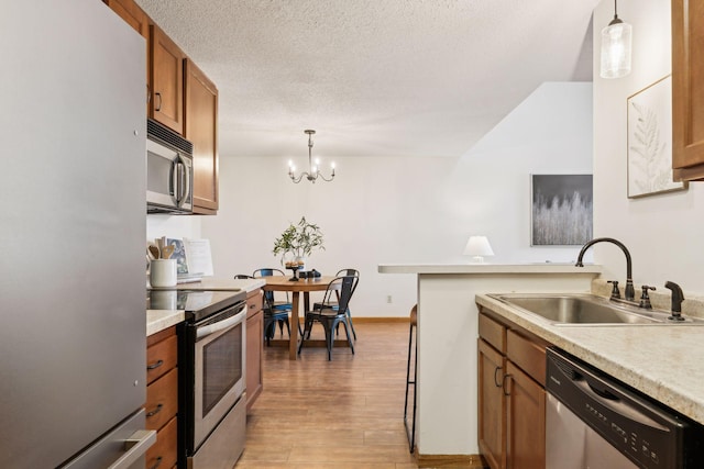 kitchen with pendant lighting, sink, light hardwood / wood-style flooring, appliances with stainless steel finishes, and a textured ceiling