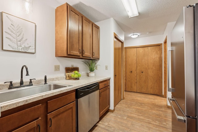 kitchen featuring sink, light hardwood / wood-style flooring, stainless steel appliances, and a textured ceiling