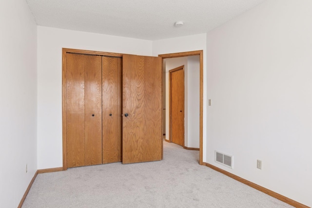 unfurnished bedroom featuring light colored carpet, a closet, and a textured ceiling