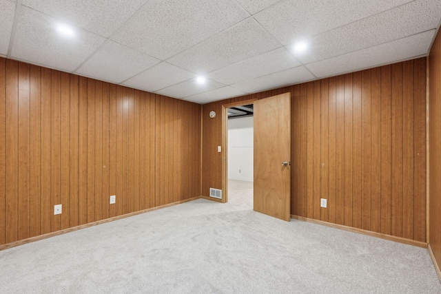 unfurnished room with light carpet, wooden walls, and a drop ceiling