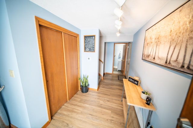 hallway featuring light wood-style floors, stairs, baseboards, and rail lighting