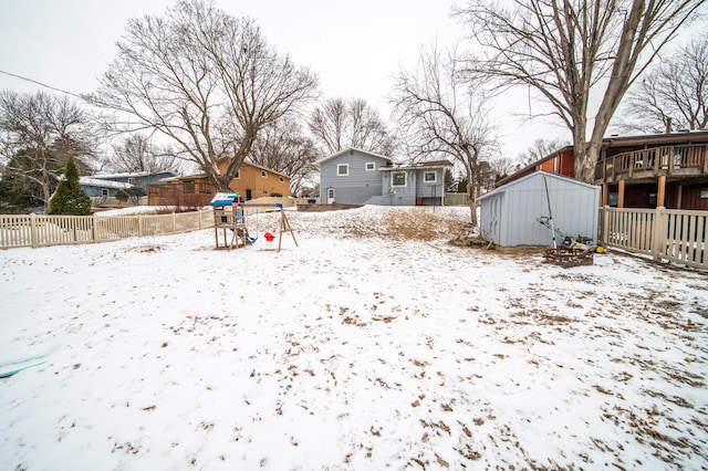 yard covered in snow with an outbuilding, a playground, fence, and a storage shed