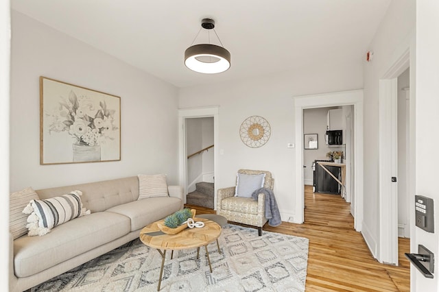 living room featuring light wood-style floors, baseboards, and stairs