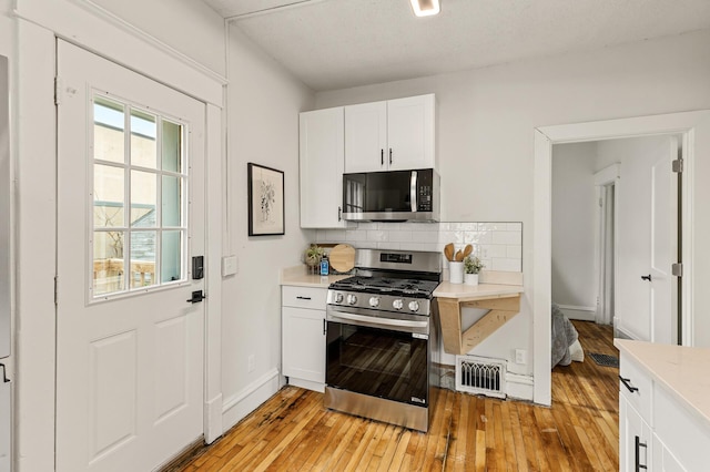 kitchen featuring appliances with stainless steel finishes, light countertops, decorative backsplash, light wood-type flooring, and visible vents