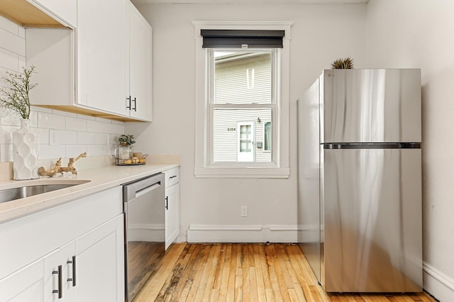 kitchen featuring light countertops, white cabinets, a baseboard radiator, light wood finished floors, and appliances with stainless steel finishes