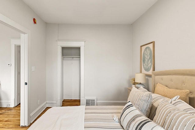 bedroom with baseboards, visible vents, wood finished floors, and a closet