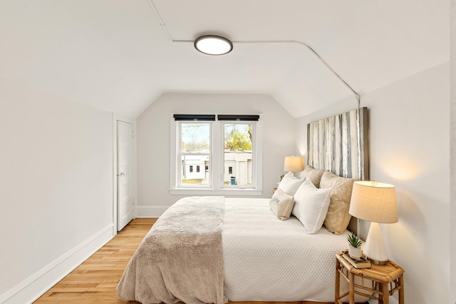 bedroom with baseboards, light wood finished floors, and vaulted ceiling