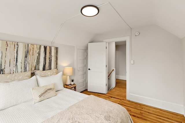 bedroom with baseboards, vaulted ceiling, and light wood-style flooring